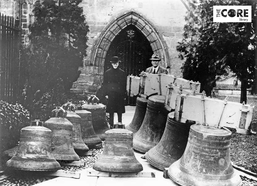 photograph of two men standing with 10 church bells in front of a church door