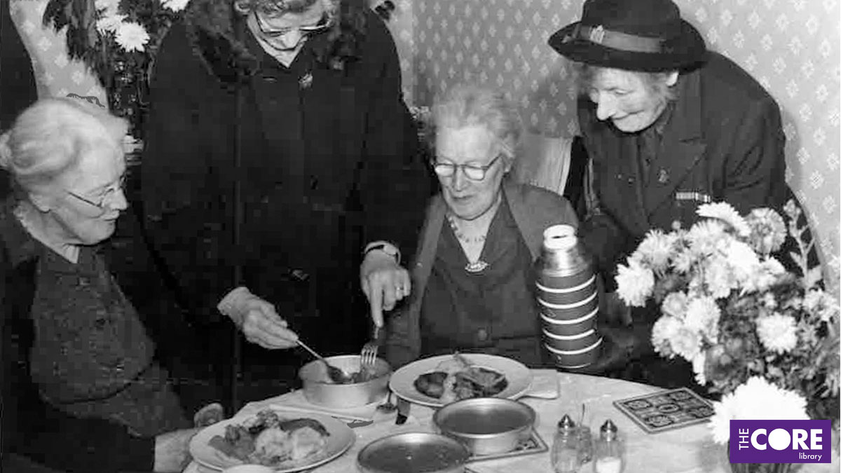 Two elderly ladies sitting at a table being served hot food by two other women