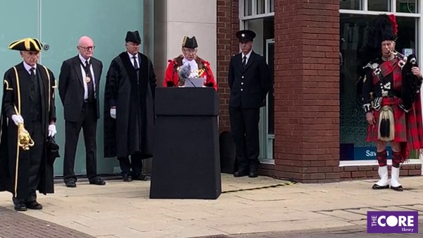 the Mayor in full regalia stands at a podium and reads from a paper